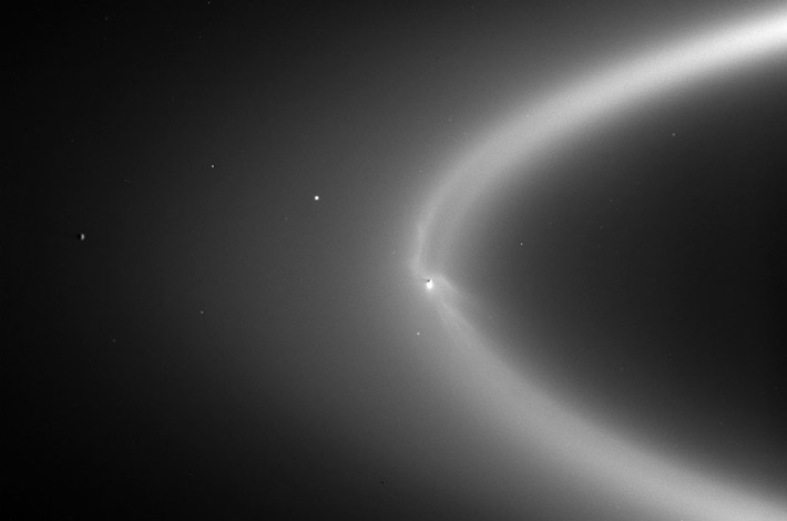 Seen as a bright arc in this 2006 observation by Cassini, Saturn's E ring is fed with icy particles from Enceladus' plume, creating wispy fingers of bright material that is backlit by the Sun. The shadowed hemisphere of the moon can be seen as a dark dot inside the ring. Credits: NASA/JPL-Caltech/Space Science Institute