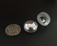 The photo shows the reflective objective lens which operates at extremely low temperatures. For size comparison, there is a 100 yen coin to the left of the two lenses.