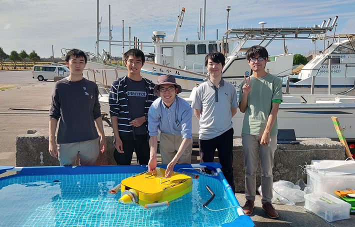 (from left) 3rd-year Systems and Control Engineering student Yo Toyomoto, Obu, Saito, Uchikawa, and Origane with their robot Kurione2