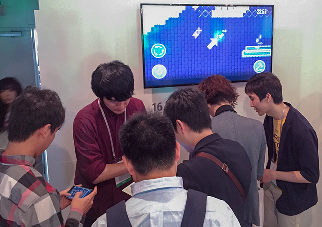 NinjaFlicker team leader Tsukasa Gotoh (burgundy shirt) and head programmer Yoshiki Ohmori (far right) introducing game at booth