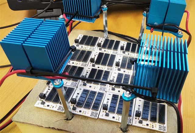 Figure 2. Experimental setup / To investigate the collective behavior of the sensors, a 4 × 4 array was prepared in the laboratory under a shielding enclosure. These sensor boards are pictured overlaying a coil connected to the exciter oscillator. Four high-power LEDs (under the blue heatsinks) provided controllable illumination, mimicking sunlight and representing the physical variable to be reconstructed from the dynamics. (Image usage restrictions: None, Image credit: Ludovico Minati)