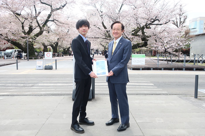 益学長へ提言書を提出する学生スタッフ代表の長谷川さん（左）