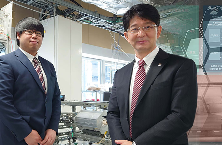 今回開発したCASBシステムの前で写真に納まる伊原学教授（右）と亀田恵佑さん（左）