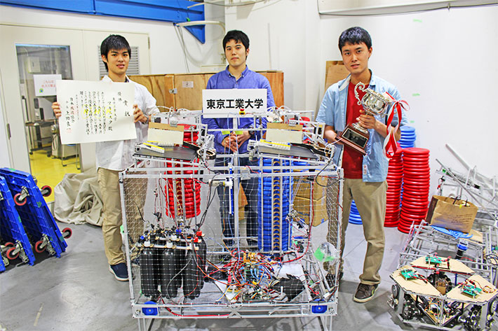 優勝したロボットとの記念撮影（左から）矢野遼人さん、徳田俊平さん、マキニスタ代表山田泰基さん