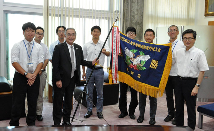 三島学長（左4番目）、 芝田政之理事・副学長（財務・施設担当）・事務局長（右1番目）と、結果報告に訪れた職員