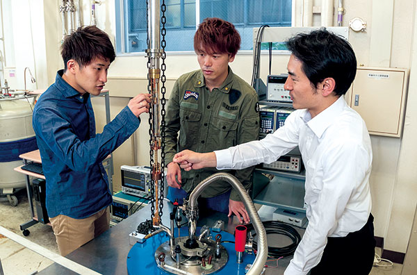 極低温状態において量子ビットの評価を行う実験の準備にとりかかる小寺准教授、田所さん、溝口さん（写真右から）。大きな磁場が必要となる実験では、こちらの大型（地下2メートル）の冷凍機を使用する。
